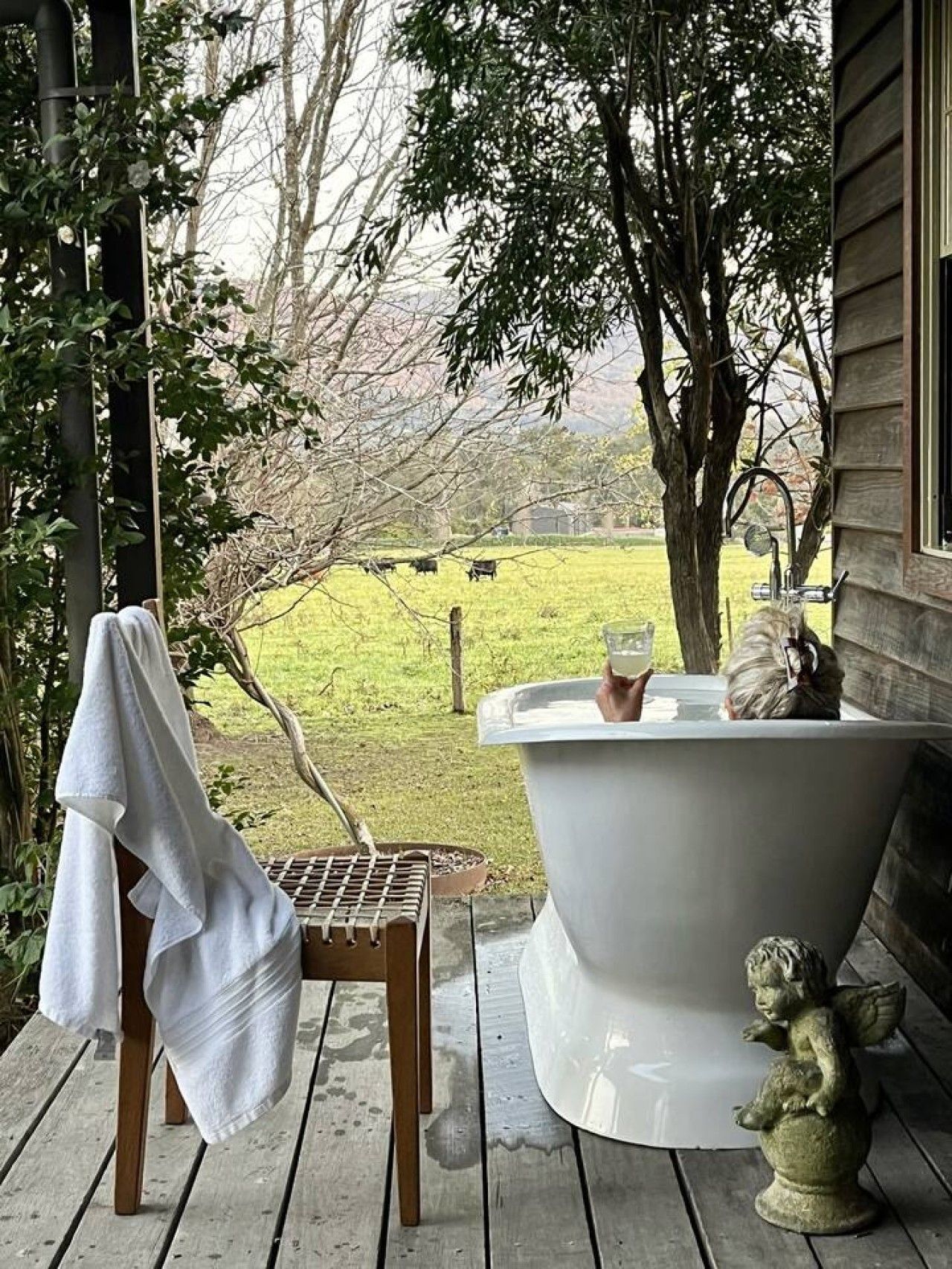 A wooden deck with a white bathtub, a white towel, and a statue.