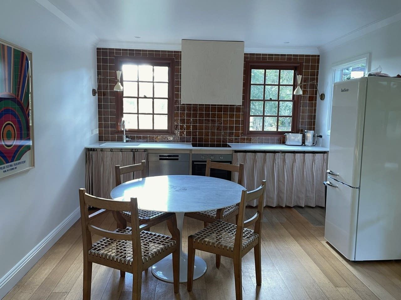 A kitchen with a round dining table, chairs, a refrigerator, and a window with curtains.