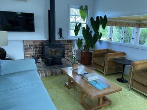 A cozy living room with a fireplace, comfortable seating, and a large window. - Architectural Cottage in heart of Kangaroo Valley (Barrengarry)
