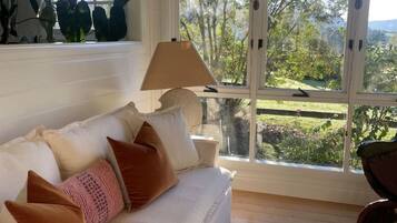 A room with a white sofa, a patterned rug, and a view of greenery outside.