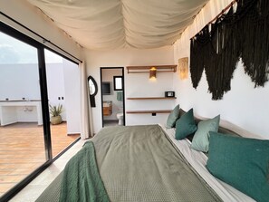 A bedroom with a bed, green pillows, a bedside table, a mirror, a hanging light fixture, and a view of the outside. - New 3BR PH Jacuzzi, Views, GYM, Pool, Cinema, WiFi (Tulum)