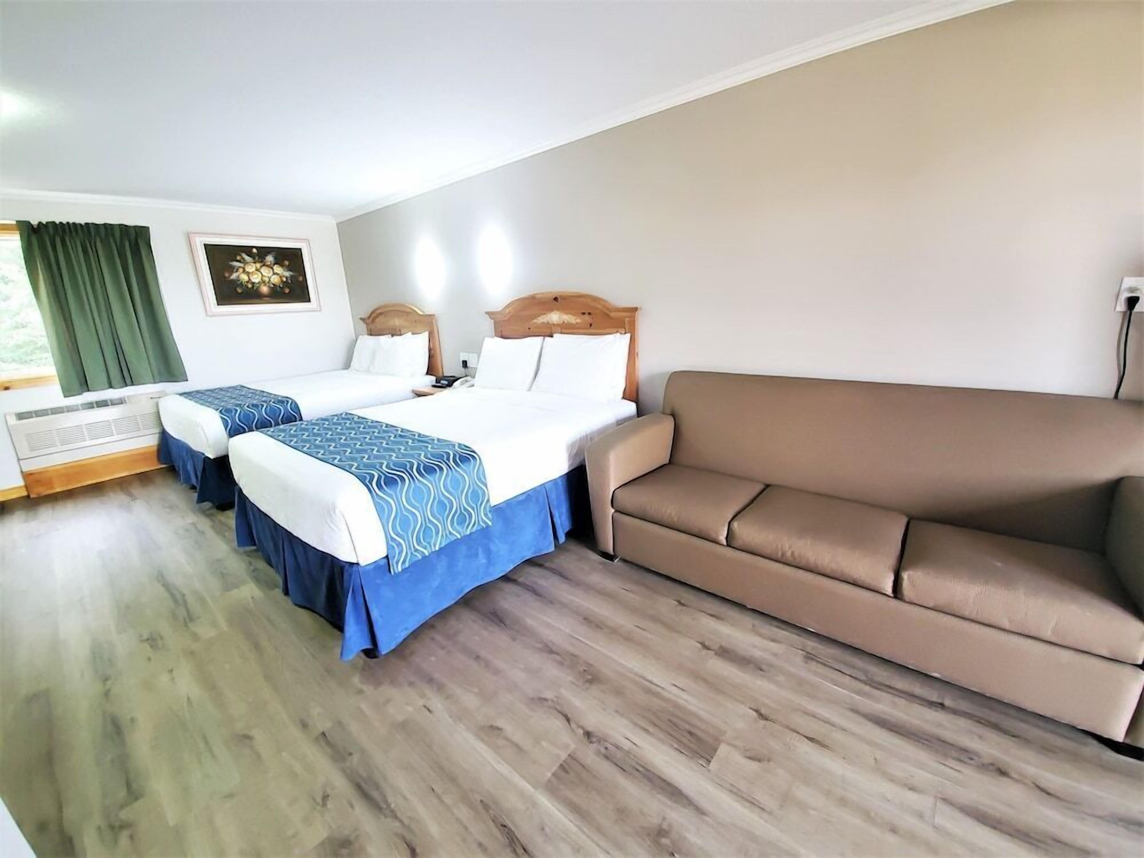 Une chambre d’hôtel avec deux lits, un canapé, un tableau au mur et une fenêtre avec des rideaux.