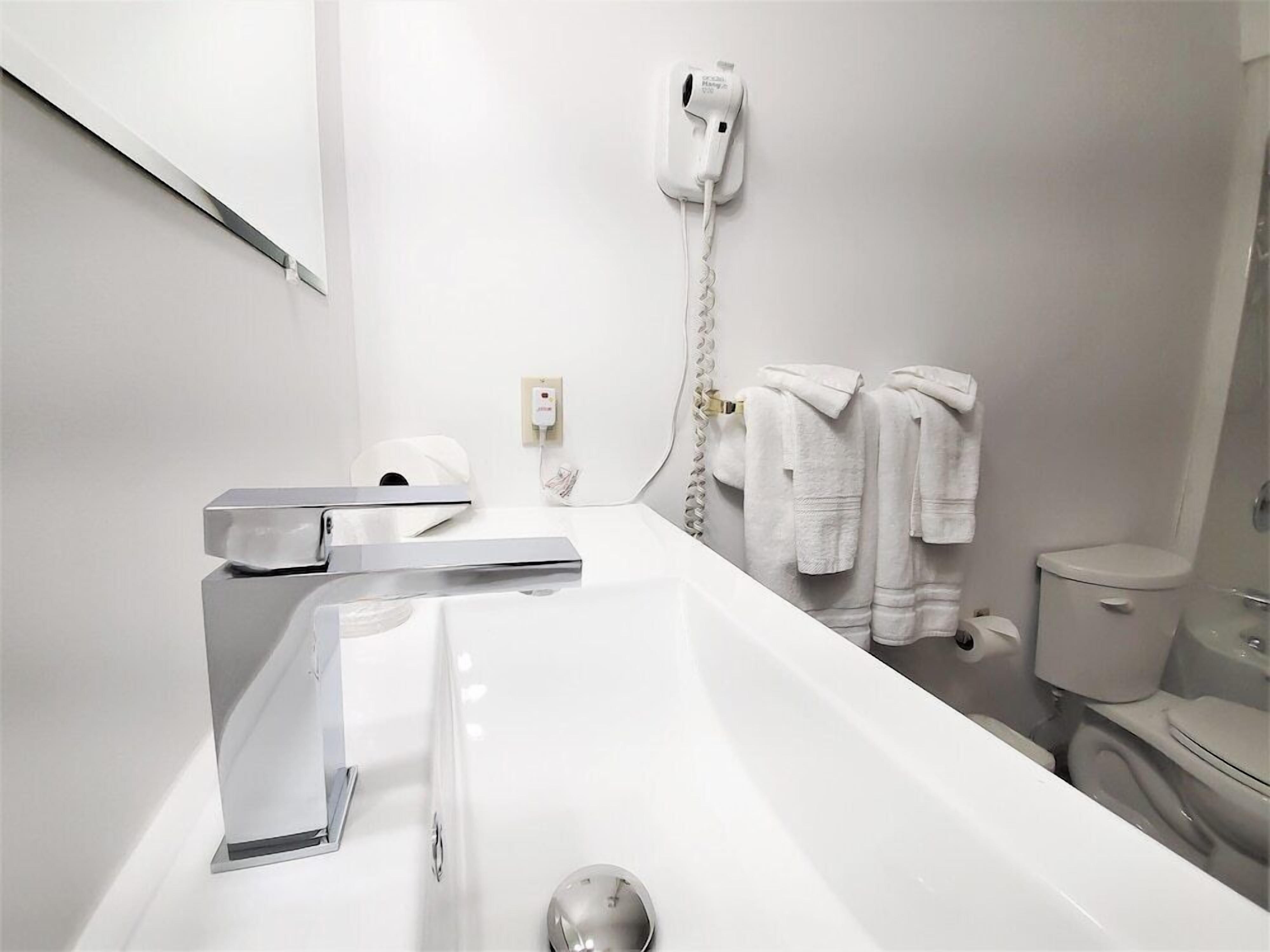 A modern bathroom with a white sink, chrome faucet, and a hairdryer mounted on the wall.