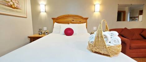 A neatly made bed with white linens, a red decorative pillow, and a wicker basket filled with towels.