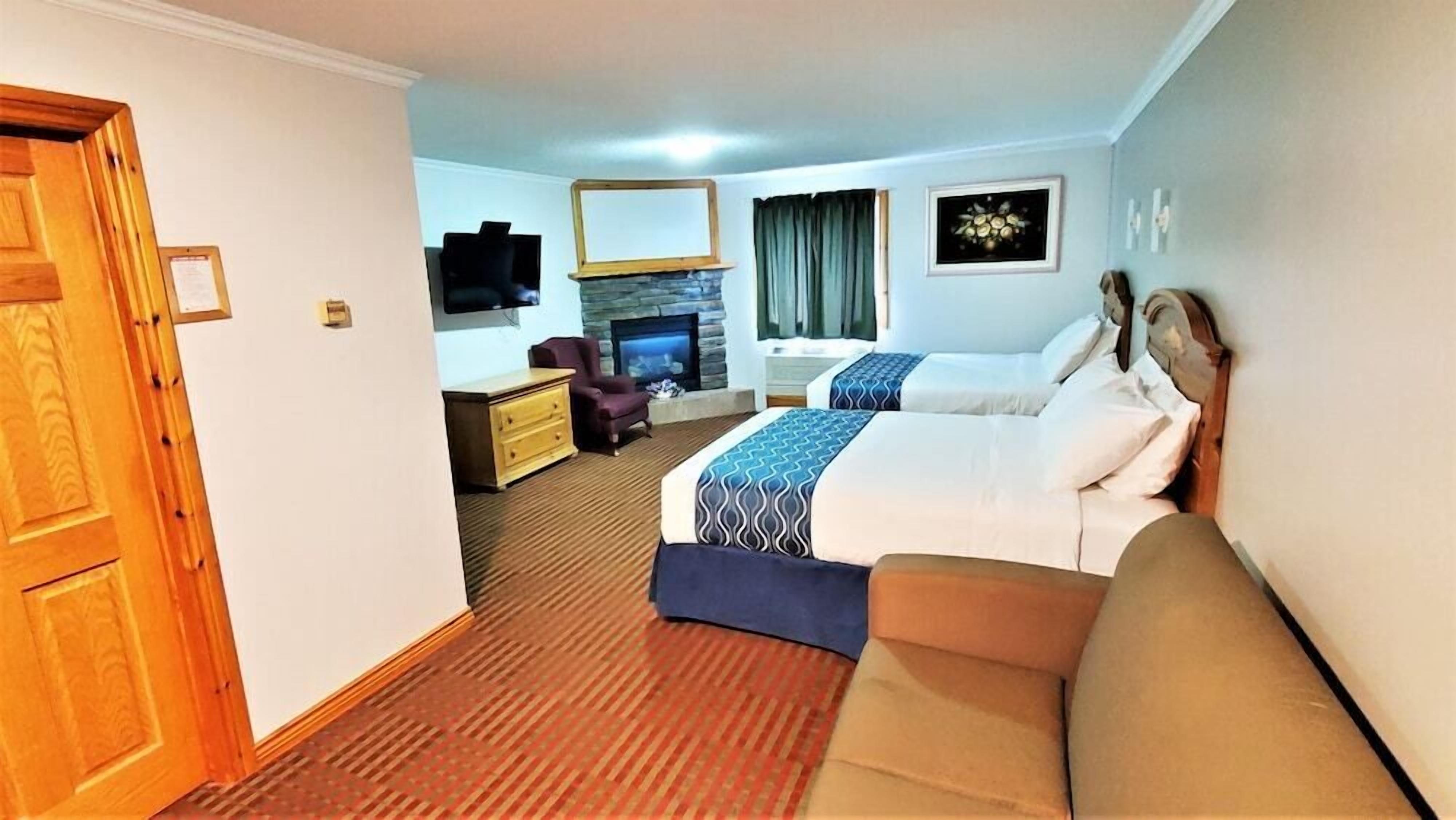 A hotel room with a wooden door, a television, a fireplace, a bed with a blue and white bedspread, a sofa, and a small desk with a chair.