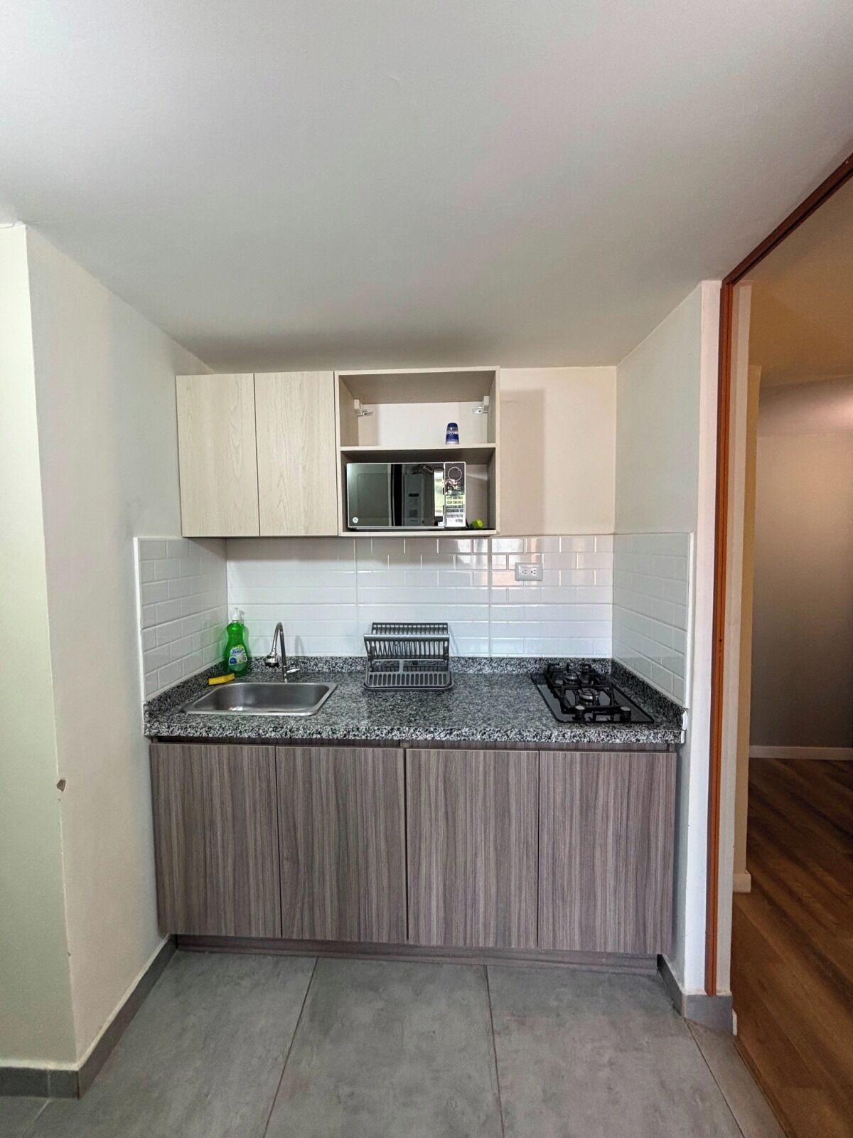 A compact kitchen with a granite countertop, a built-in microwave, and a stainless steel sink.