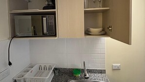 A kitchen with a granite countertop, a stainless steel sink, a microwave, and a cabinet with a coffee maker. - ApartaHotel Retiro 79 (Bogotá)