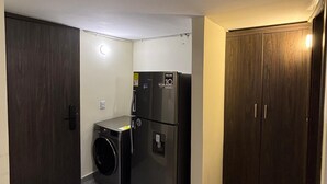 A compact kitchen with a washing machine, a refrigerator, and a dark wooden wardrobe. - ApartaHotel Retiro 79 (Bogotá)