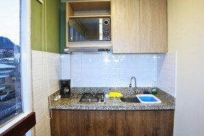 Uma cozinha compacta com micro-ondas, cafeteira, fogão a gás, pia e janela com vista para a cidade.