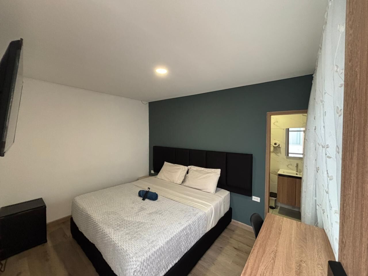 A bedroom with a bed, a bedside table, a nightstand, a mirror, and a bathroom visible through an open door.