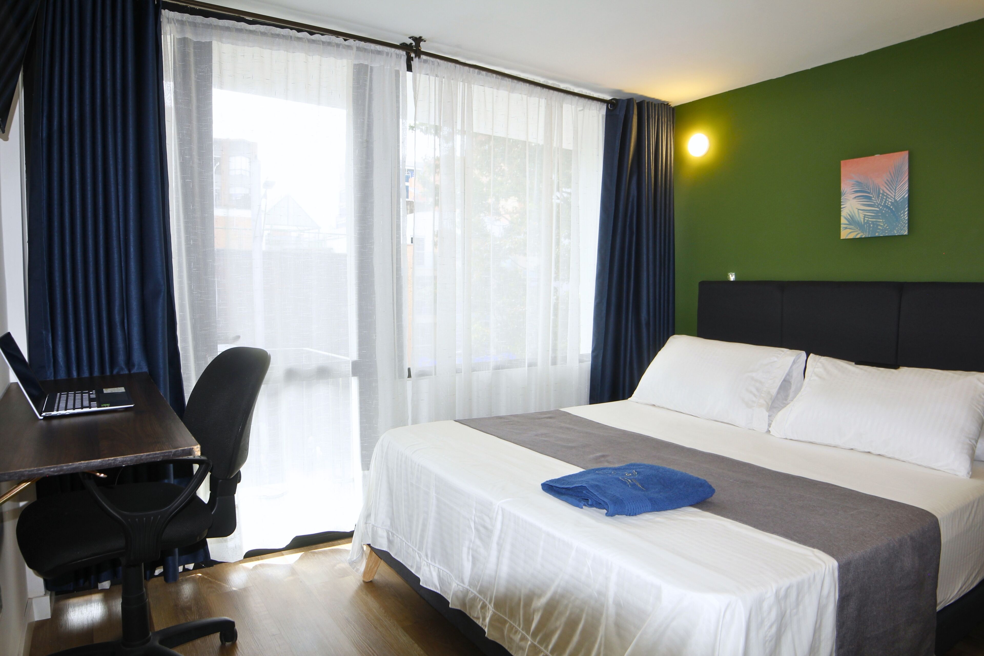 Une chambre d’hôtel avec un lit, un bureau avec un ordinateur portable, une chaise et une fenêtre avec des rideaux.
