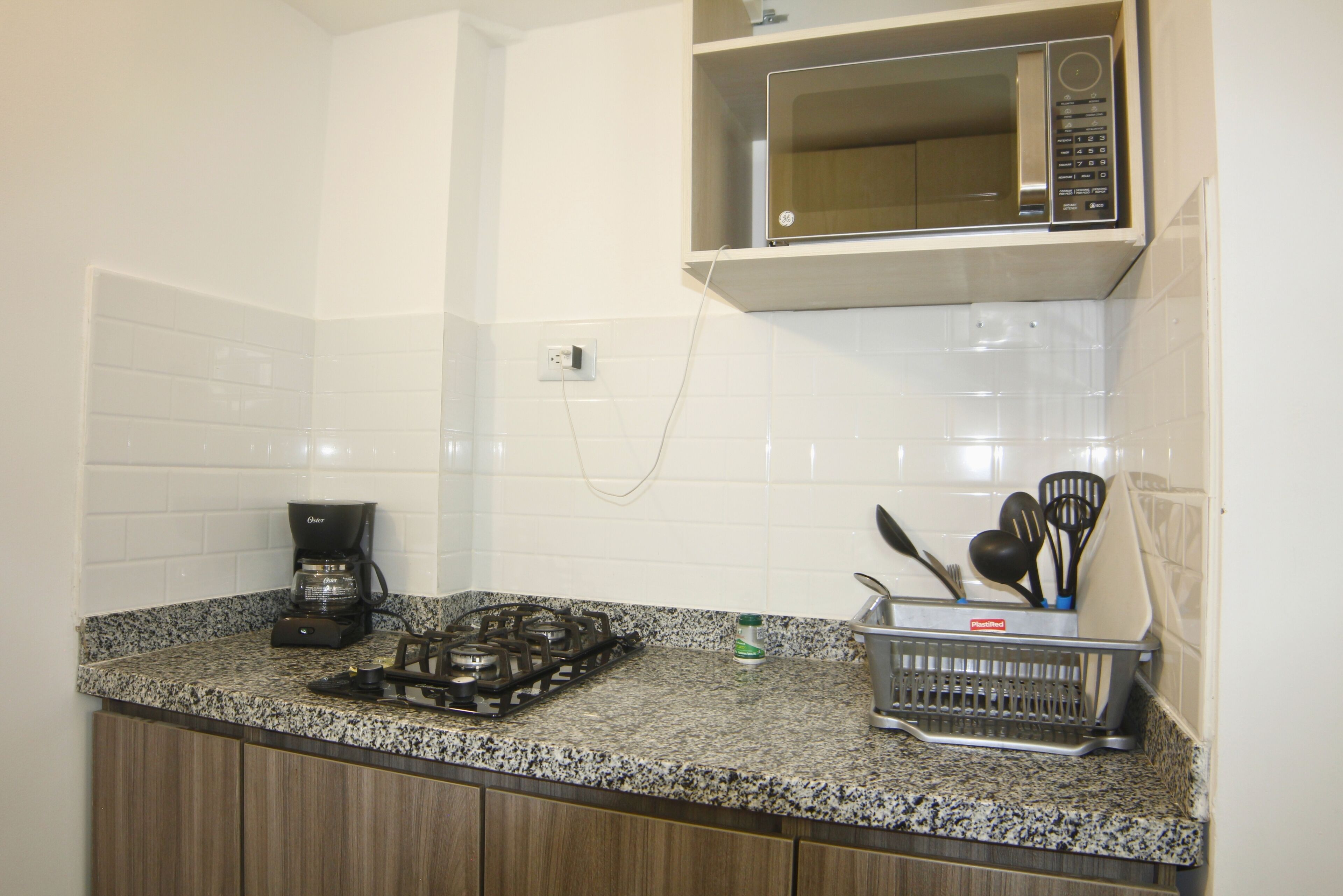 A kitchen with a gas stove, a coffee maker, a microwave, and a dish rack with utensils.