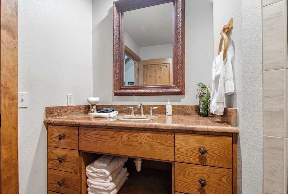 Een badkamer met een houten wastafelmeubel, een spiegel, een wastafel en een handdoekrek.