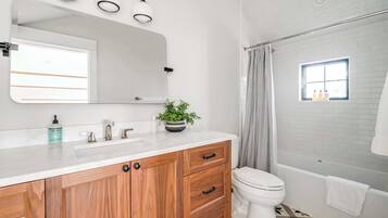 Un baño moderno con un tocador blanco, armarios de madera, un inodoro y una zona de ducha.