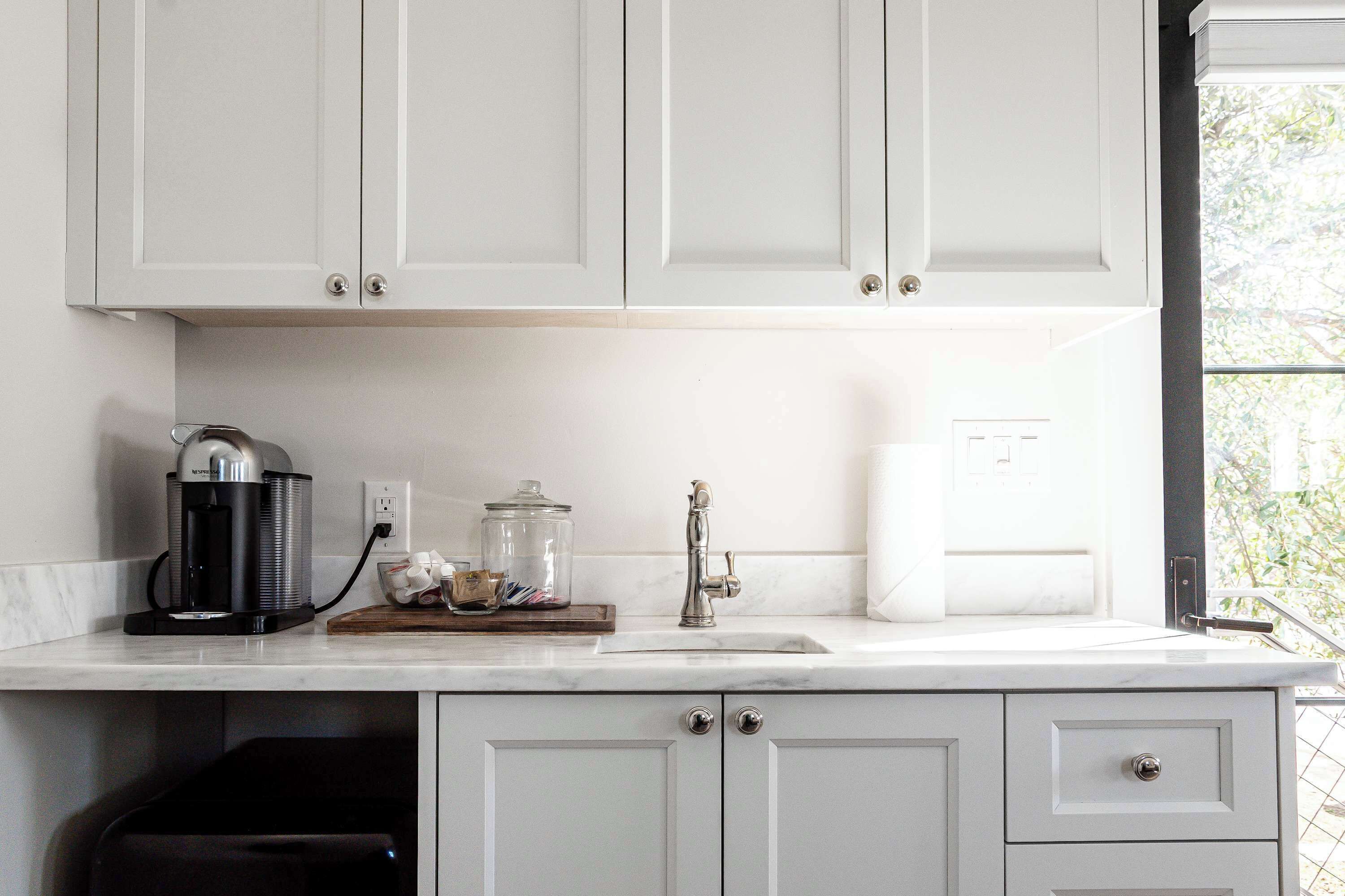A kitchen with white cabinets, a coffee maker, a glass jar, and a sink.