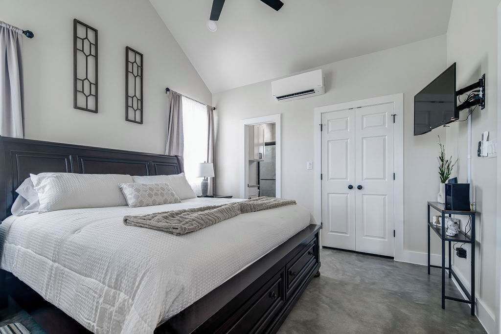 A bedroom with a large bed, a TV mounted on the wall, and a wardrobe.