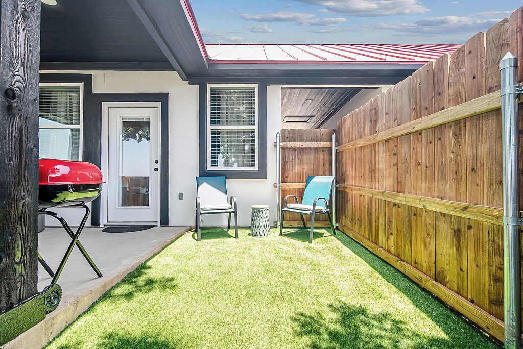 A backyard with a wooden fence, a red grill, and two chairs.