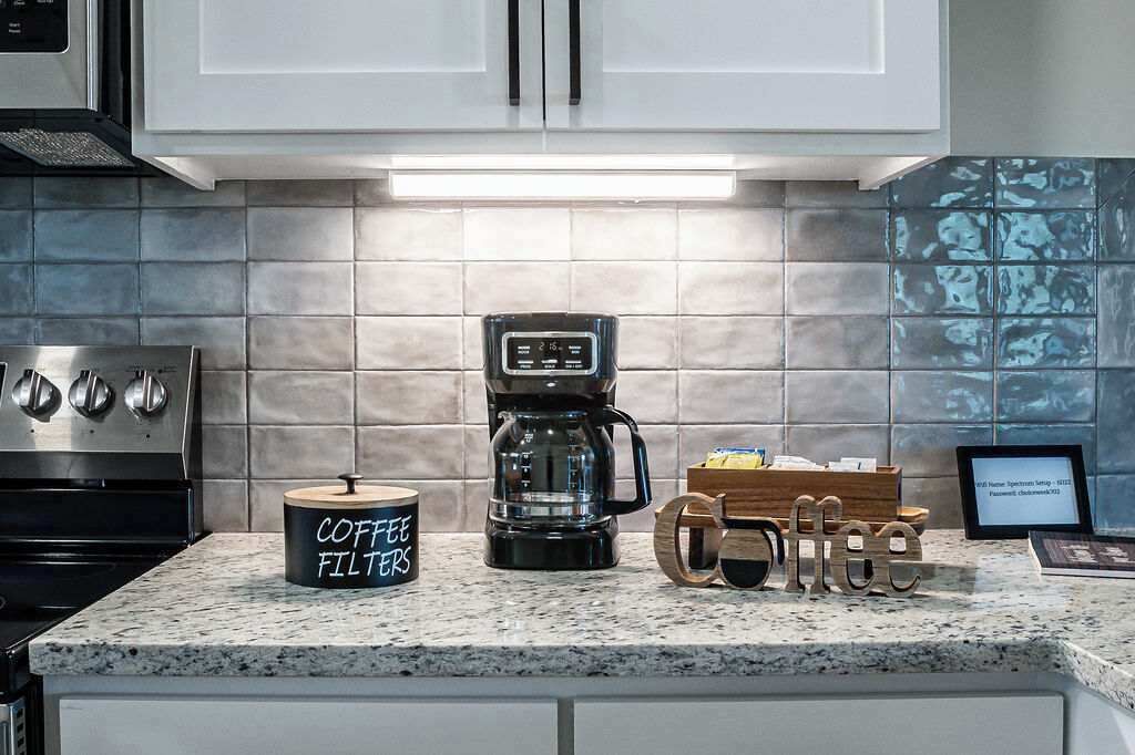Una cocina con armarios blancos, una cafetera, un recipiente para filtro de café y decoraciones de madera con temática del café.
