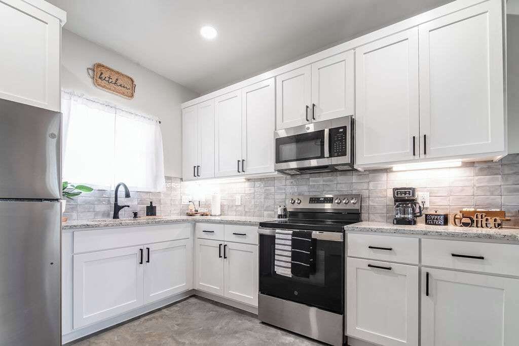 A modern kitchen with white cabinets, stainless steel appliances, and a window with a white curtain.