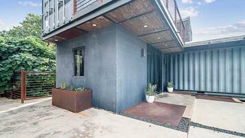 A modern building with a grey facade, a small window, and a concrete patio area with potted plants.