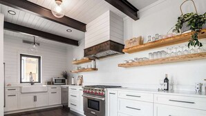 Una cocina moderna con armarios blancos, estufa de acero inoxidable, estantes de madera y una planta colgante.