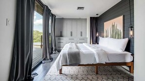 Un dormitorio con cama, armario y un amplio ventanal con cortinas.