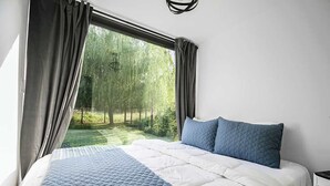 Un dormitorio con una cama grande, cortinas grises y vistas a un jardín.