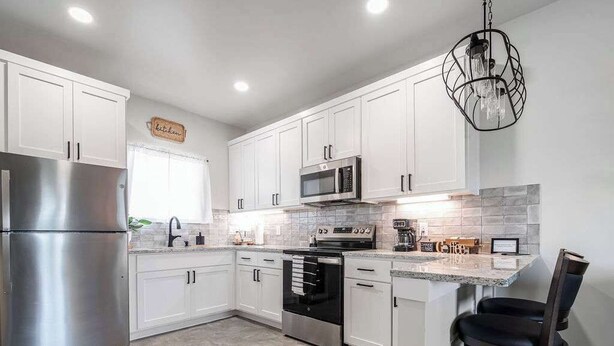 A modern kitchen with white cabinets, stainless steel appliances, a granite countertop, and a hanging light fixture. - Live Oak Cabins-sleeps 8 W/hot-tubs (Fredericksburg)