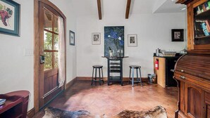 Ein geräumiges Zimmer mit Holztür, einem Esstisch mit Hocker, einem Kamin und einem Bücherregal.