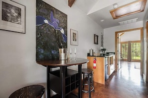 A modern kitchen with a wooden table, bar stools, and a large painting of a blue flower. - The Manor Haus at Messina Hof Hill Country Winery-paris Haus (Fredericksburg)