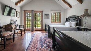 Ein Schlafzimmer mit einem großen Bett, einem Schreibtisch, einem Sessel, einem Fernseher und einem Fenster mit Blick auf Grünflächen.