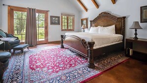 Une chambre avec un grand lit, un bureau et une chaise, offrant une vue sur les arbres à travers les fenêtres.