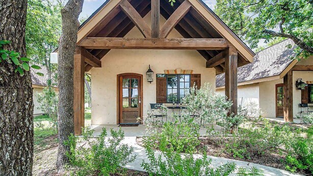 Un chalet rustique doté d’une véranda en bois, d’une cheminée en pierre et d’un jardin.