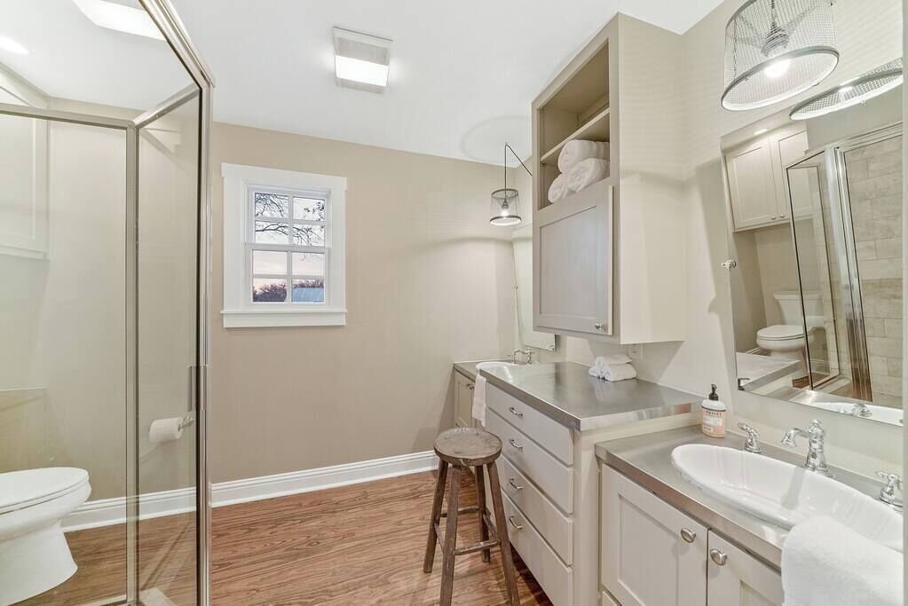 A modern bathroom with a glass shower enclosure, a vanity with a sink and mirror, and a window with a view.