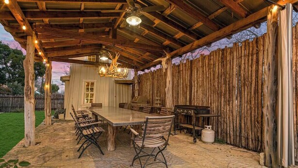 Une terrasse extérieure avec un sol en pierre, des meubles en bois et une clôture en bois rustique.