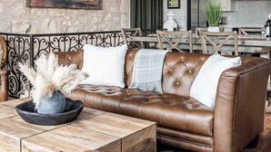 A living room with a brown leather sofa, a wooden coffee table, and a chandelier. - The Bank-luxury Suite W/deck Overlooking Main St! (Fredericksburg)