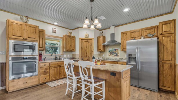 Uma cozinha com armários de madeira, eletrodomésticos de aço inoxidável, uma ilha central com banquetas e iluminação embutida no teto.