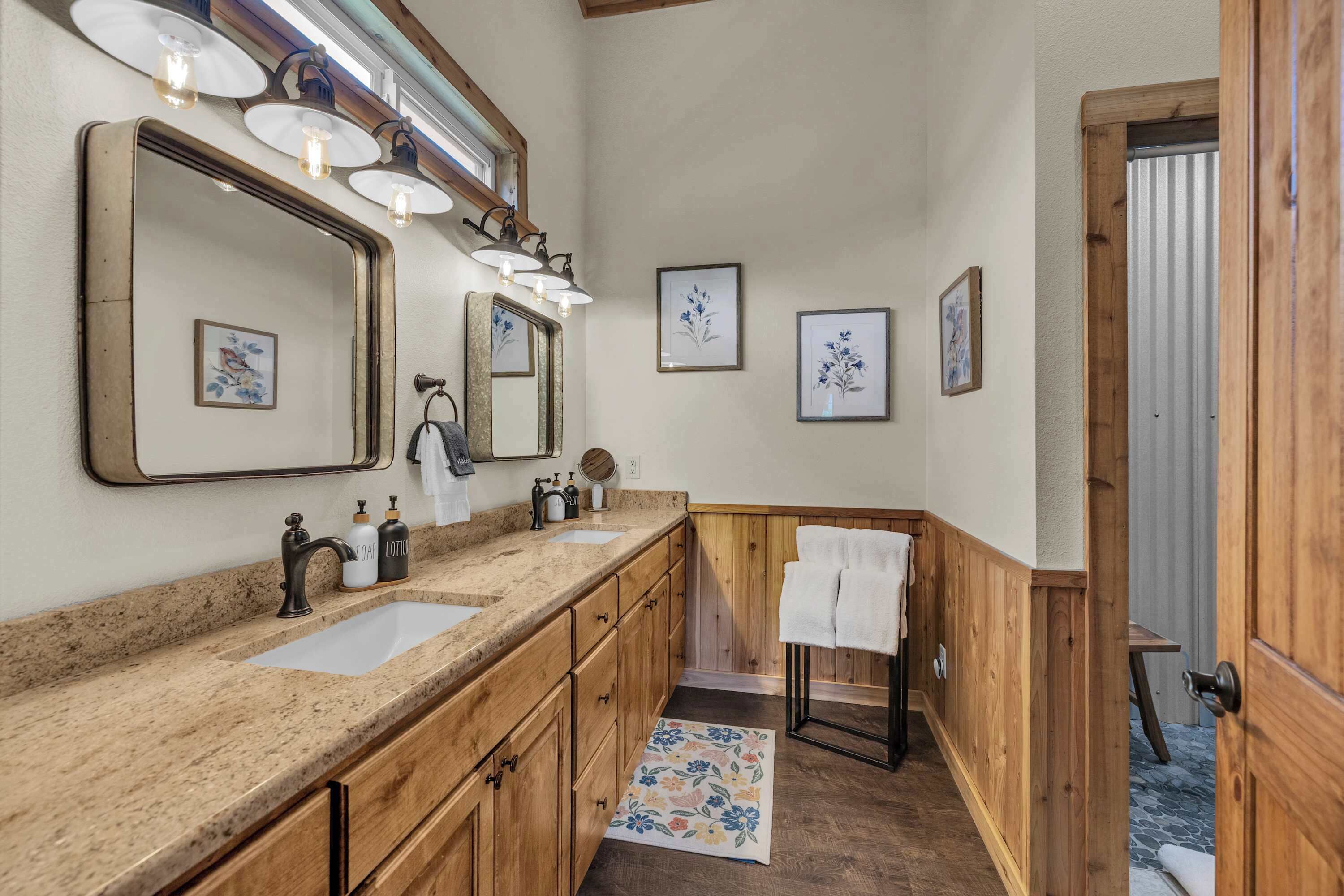 Un bagno con mobili in legno, un ampio specchio, due lavandini e un quadro floreale incorniciato appeso al muro.
