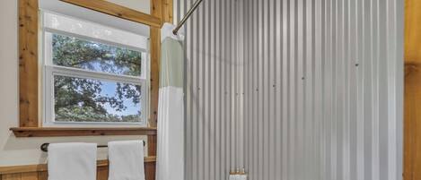A bathroom with a wooden vanity, a bathtub, and a window with a view of trees.