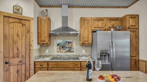 Uma cozinha com armários de madeira, uma geladeira de aço inoxidável, bancada de mármore e uma garrafa de vinho.