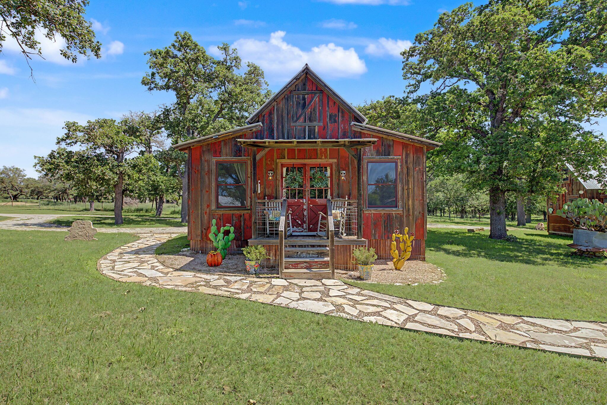 A rustic wooden cabin with a stone pathway leading to the entrance, surrounded by greenery.