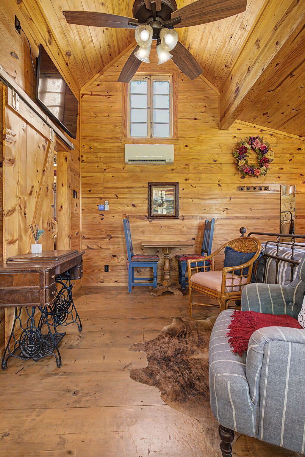Een knus interieur van een chalet met een houten plafond, een plafondventilator, een eettafel, twee stoelen, een bank en een vloerkleed.