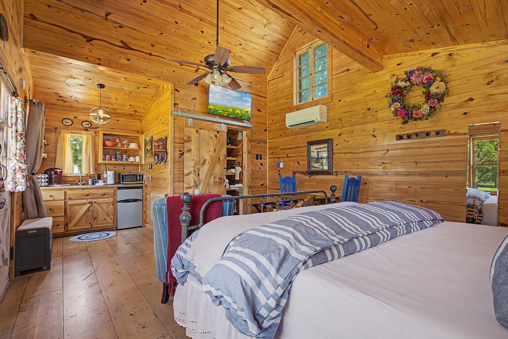 A cozy log cabin bedroom with a large bed, a ceiling fan, and a view of the outdoors through a window.