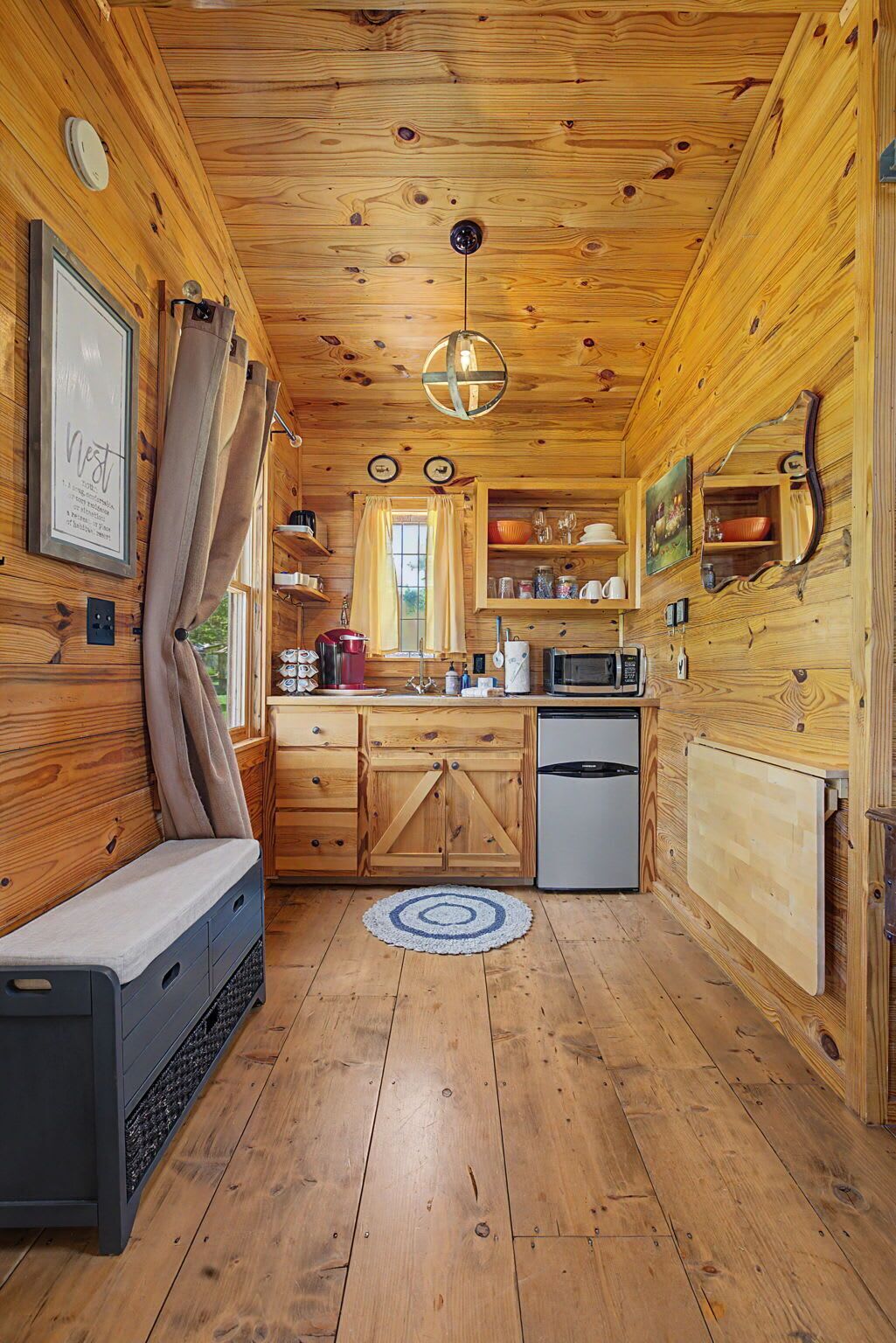 A wooden cabin interior with a kitchenette, a dining area, and a sleeping area.