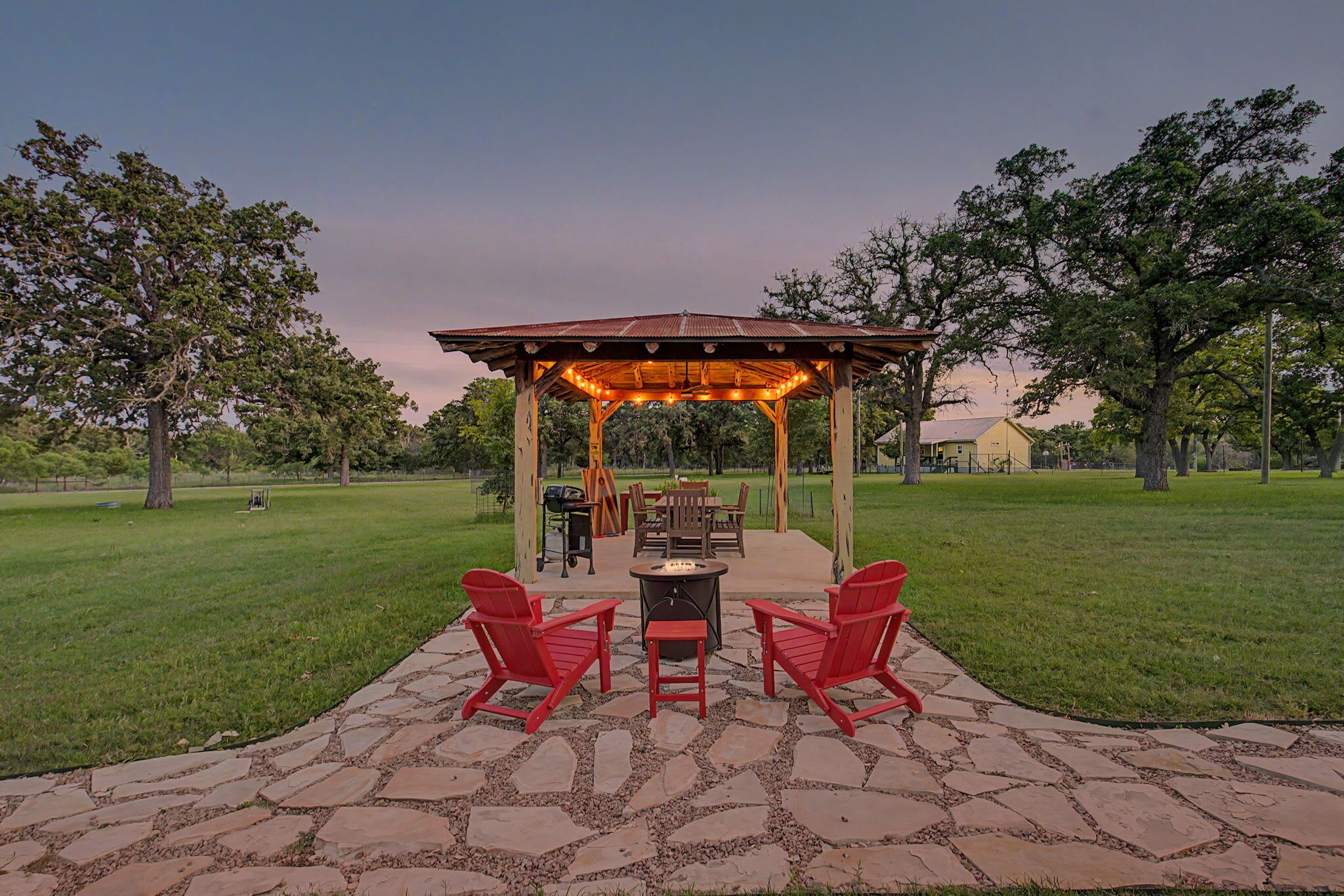 Un jardín con glorieta, una chimenea y zona de estar, rodeado de un patio de piedra.