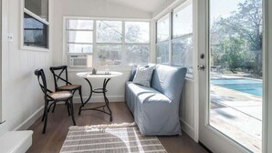 A sunroom with a pool view, a seating area with a sofa and chairs, and a small table with a lamp. - Suniland W/pool, Hot-tub and Sauna! (Fredericksburg)