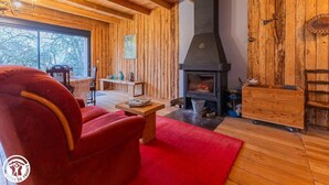 A cozy wooden interior with a fireplace, red furniture, and a view through the window.
