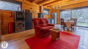 A cozy cabin interior with a red sofa, wooden floors, a kitchen area, and a dining table with chairs.