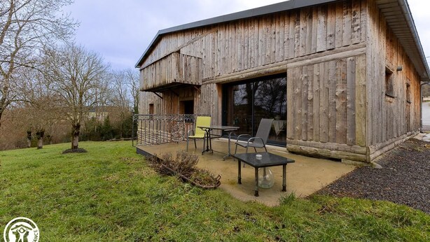 A rustic wooden building with a balcony and a patio area with outdoor seating.