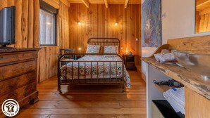 A cozy wooden cabin bedroom with a bed, bedside tables, a dresser, and a large window.